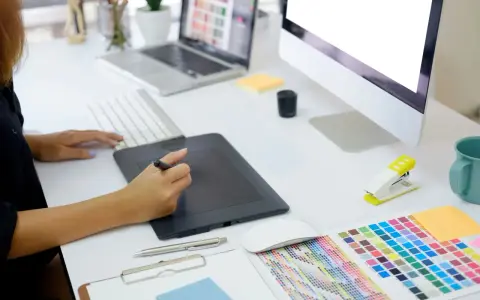 En grafisk designer arbetar vid sitt skrivbord med en ritplatta, tangentbord och en färgkarta. En bra **concept vista prisjakt** för kreativa projekt.