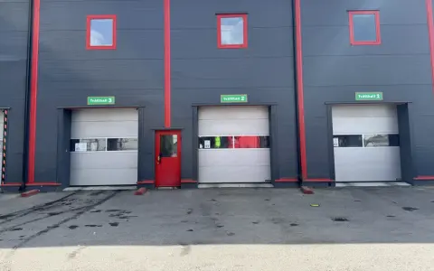 Grå fasad med röda detaljer och tre portar märkta Tvätthall 1, 2 och 3. En röd dörr finns mellan portarna.