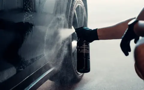 En hand med handske sprayar en bil för att ta bort dekaler.