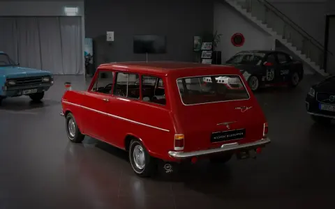 Röd veteranbil med ålder, en Opel Caravan, står i en bilhall bredvid en blå bil och en tävlingsbil.