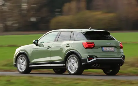 Grön Audi Q2 kör på en landsväg, med suddiga träd och fält i bakgrunden. Kanske ett audi q2 problem med att den kör för fort?