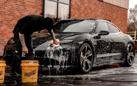 Person tvättar en svart bil med Autoglym-produkter. Två gula hinkar står bredvid.