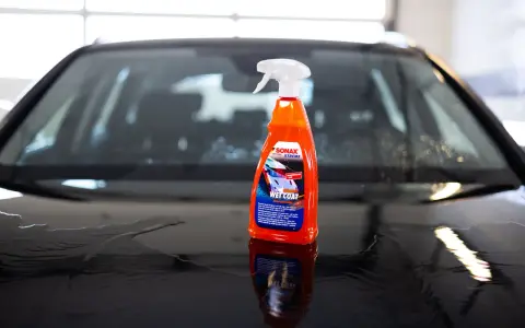 En flaska SONAX Xtreme Ceramic Wet Coat står på en våt bilhuv.
