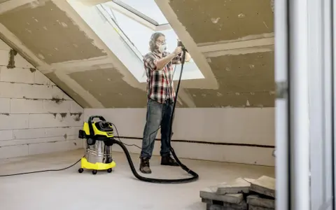 Man med skyddsutrustning använder Kärcher WD 6 för att dammsuga vid renovering av ett vindsrum.