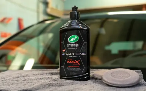 En flaska Turtle Wax Hybrid Solutions Pro Graphene Infused Wax, ett bilschampo för maximal glans och skydd, ligger på en grå handduk.
