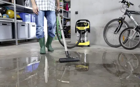 Man i gröna stövlar använder Kärcher WD 6 P Premium för att suga upp vatten på ett betonggolv i ett garage.