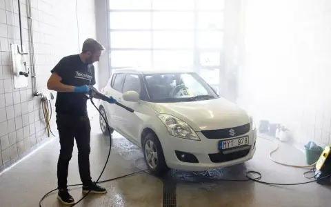 Man med högtryckstvätt gör bilen skinande ren. En riktig asfaltslösare som får bort all smuts.