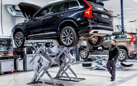 Mekaniker arbetar med en svart Volvo på en billyft i en auktoriserad verkstad.