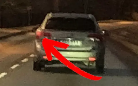 En röd pil pekar på bakljuset på en bil. Det är mörkt ute, och man undrar om man måste ha bakljus på dagen.