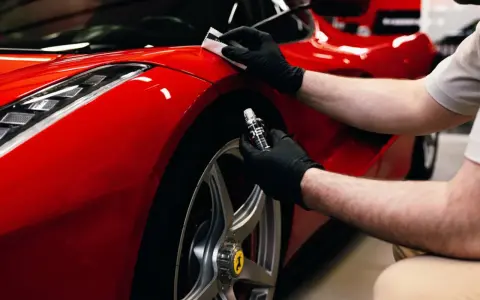 En person med svarta handskar applicerar en skyddande beläggning, troligen **Hydrosilex**, på en röd Ferrari.