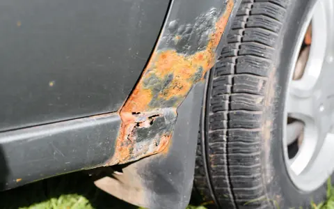 Rostfläckar och skador på bilens skärm nära däcket. En del av lacken har bubblat sig och metallen är synlig. Dags att ta bort repor på bilen och fixa rosten!