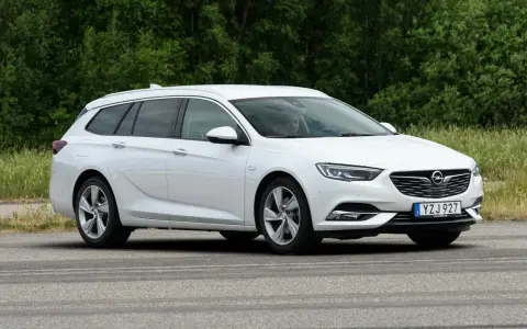Vit Opel Insignia kombi parkerad vid en grönskande skog. En förare syns i bilen, kanske funderar på ett opel insignia problem.