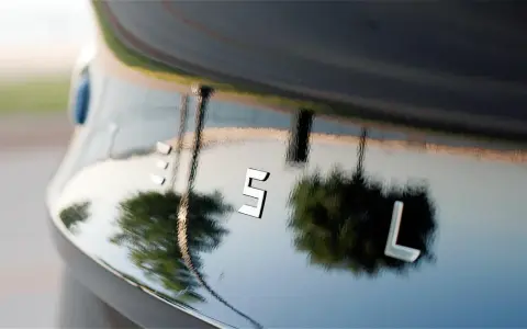 Bilens blanka lack, som en apelsinskal, reflekterar träd och himmel. Bokstäverna "ES L" syns tydligt.