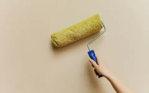 En hand håller en färgroller med gul päls, redo att måla en vägg. Kanske är det dags för en 3m rubbing för att fräscha upp hemmet.