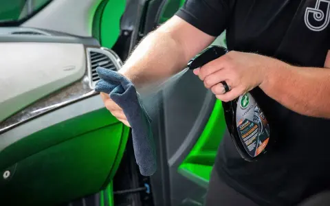 Person sprayar en trasa med en produkt för bilvård, en effektiv wax remover, för att rengöra bilens interiör.