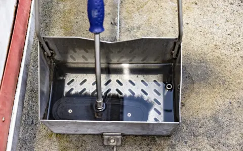 En borste med blått handtag vilar i en vattenfylld smutsavskiljare av metall.