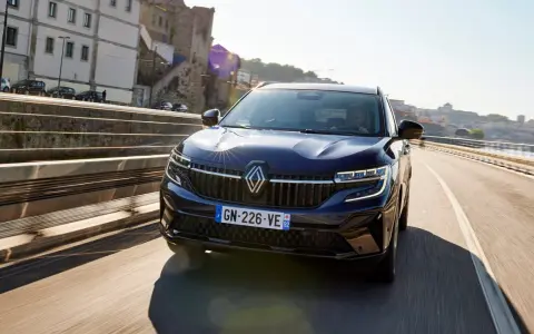 Mörkblå Renault Koleos kör på en bro i solsken. Inga problem syns med bilen.