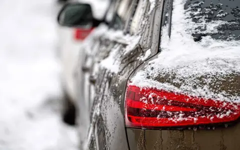 En mörk bil täckt av snö och is. En perfekt dag för ett bilvårdspaket för att få bilen skinande ren igen.