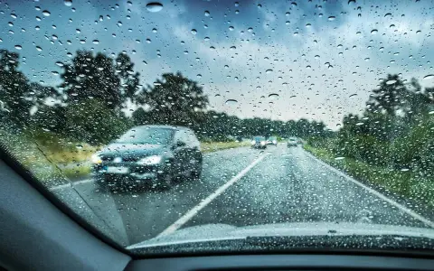 Regndroppar på vindrutan. Bilar kör på en väg genom ett trädbevuxet landskap. Glaco-behandlingen håller sikten klar.