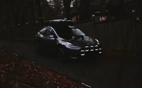 Mörk Tesla med takbox och extraljusstag redo för äventyr längs en höstfärgad väg.