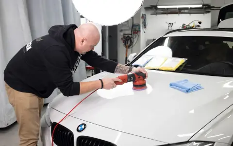 Man polerar en vit bil med en polermaskin, använder Menzerna-produkter för en perfekt finish.