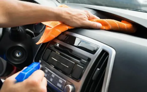 En hand sprayar och torkar av bilens instrumentbräda med en orange trasa. Det ser ut som en magisk rengöring för att få bilen skinande ren.