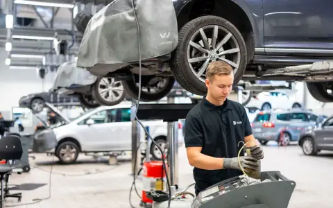 Mekaniker arbetar med en bil på en verkstad. Frågan "hur lång tid tar en bilservice" kan variera beroende på vad som behöver göras.