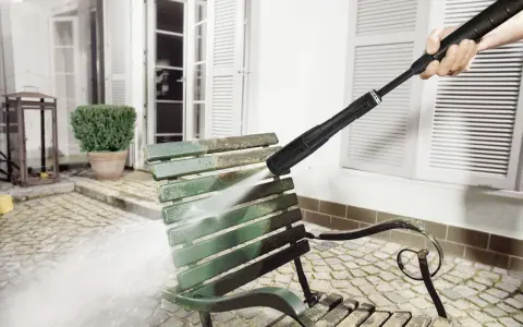 En Kärcher K5 rengör en smutsig grön parkbänk utomhus.