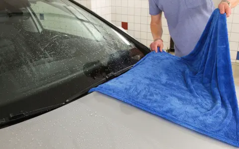 En person torkar av en bilruta med en blå torkhandduk.