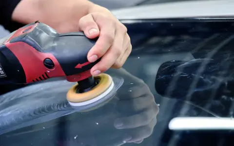En hand polerar en bilruta med en polermaskin. Glaspolish ger en perfekt finish.