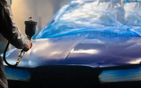 Person lackar om bilen billigt med sprutpistol. Bilen är täckt med blå plast.
