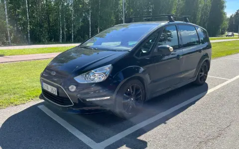 Svart Ford S-Max med takräcke parkerad på en asfalterad yta. En liten bit av stötfångaren verkar vara skadad, ett potentiellt **Ford S-Max problem**.