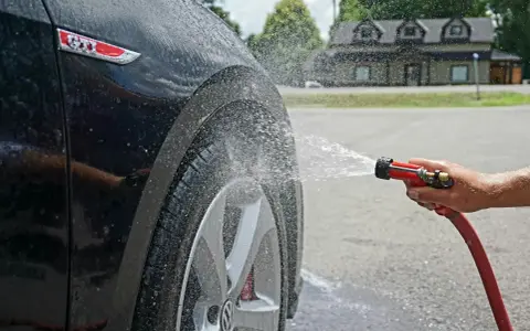 Tvätta bilen hemma medel. Vatten sprutar på en svart GTI-bil.