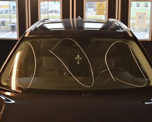 En flammig bilruta med ett kors som hänger från backspegeln.