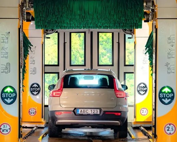 Volvo XC40 i en automatisk biltvätt med autoclean + wax-program. Gröna borstar hänger redo för en skinande ren bil.