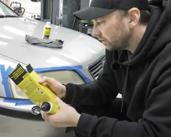 Man förbereder polering strålkastare biltema. En flaska med produkt och trasa ligger på bilen.