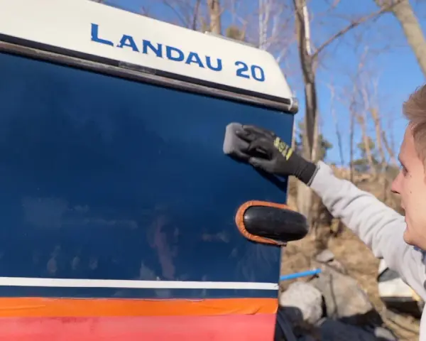 Man applicerar keramisk lackskyddsbehandling på en blå båt med texten "LANDAU 20".