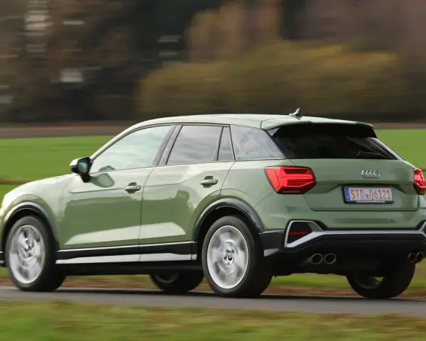 Grön Audi Q2 kör på en landsväg, med suddiga träd och fält i bakgrunden. Kanske ett audi q2 problem med att den kör för fort?