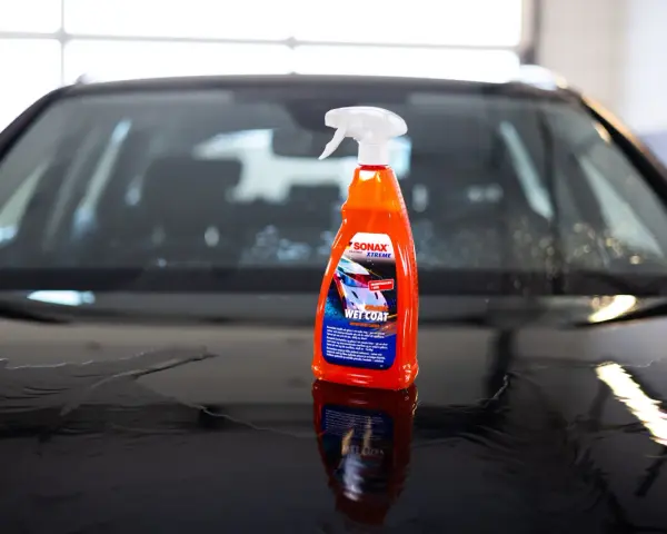 En flaska SONAX Xtreme Ceramic Wet Coat står på en våt bilhuv.