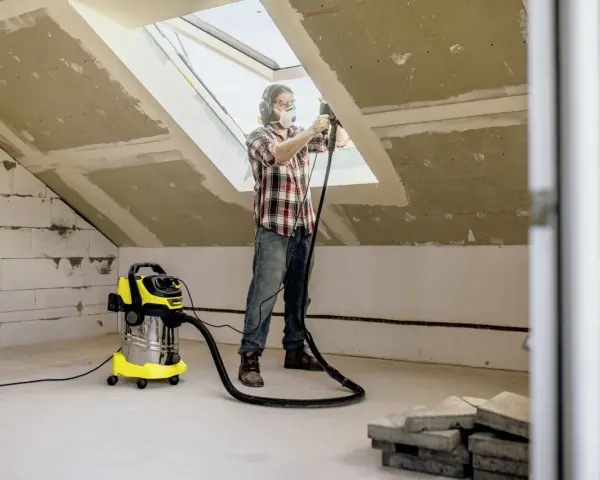Man med skyddsutrustning använder Kärcher WD 6 för att dammsuga vid renovering av ett vindsrum.