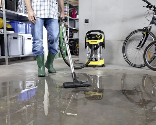 Man i gröna stövlar använder Kärcher WD 6 P Premium för att suga upp vatten på ett betonggolv i ett garage.