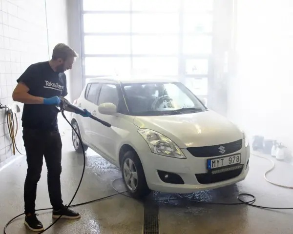 Man med högtryckstvätt gör bilen skinande ren. En riktig asfaltslösare som får bort all smuts.