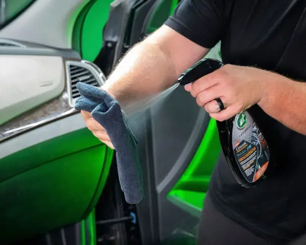 Person sprayar en trasa med en produkt för bilvård, en effektiv wax remover, för att rengöra bilens interiör.