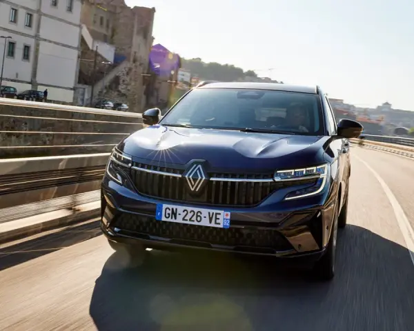 Mörkblå Renault Koleos kör på en bro i solsken. Inga problem syns med bilen.