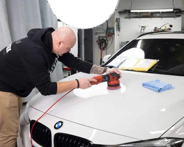 Man polerar en vit bil med en polermaskin, använder Menzerna-produkter för en perfekt finish.