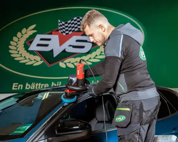 Man polerar en bil med polermaskin. En professionell rekond bil-tjänst som ger nytt liv åt lacken.