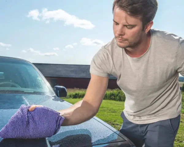 Man puts the finishing touches on his car with a waterless wash, leaving a sparkling shine under a blue sky.