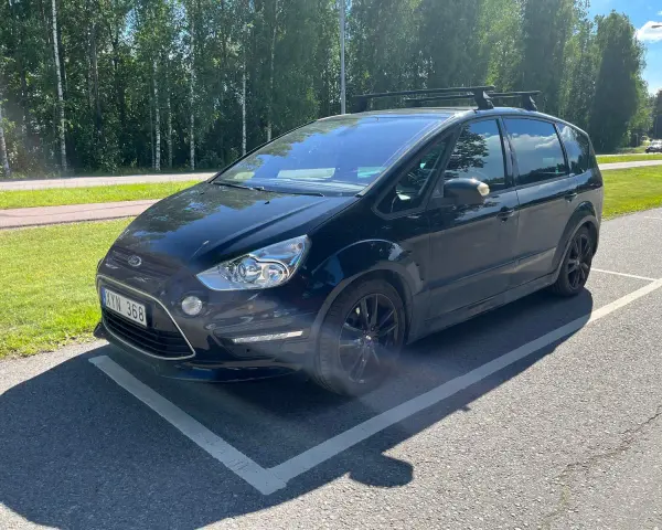 Svart Ford S-Max med takräcke parkerad på en asfalterad yta. En liten bit av stötfångaren verkar vara skadad, ett potentiellt **Ford S-Max problem**.