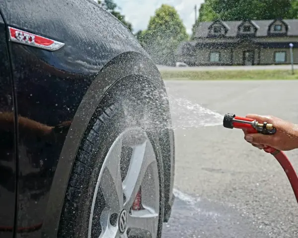 Tvätta bilen hemma medel. Vatten sprutar på en svart GTI-bil.