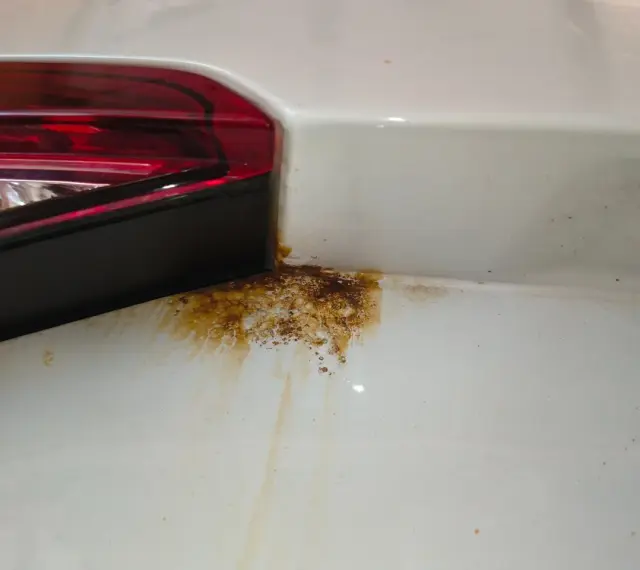 Rostfläckar vid bakljuset på en vit bil. Dags att laga rost bil innan det blir värre.